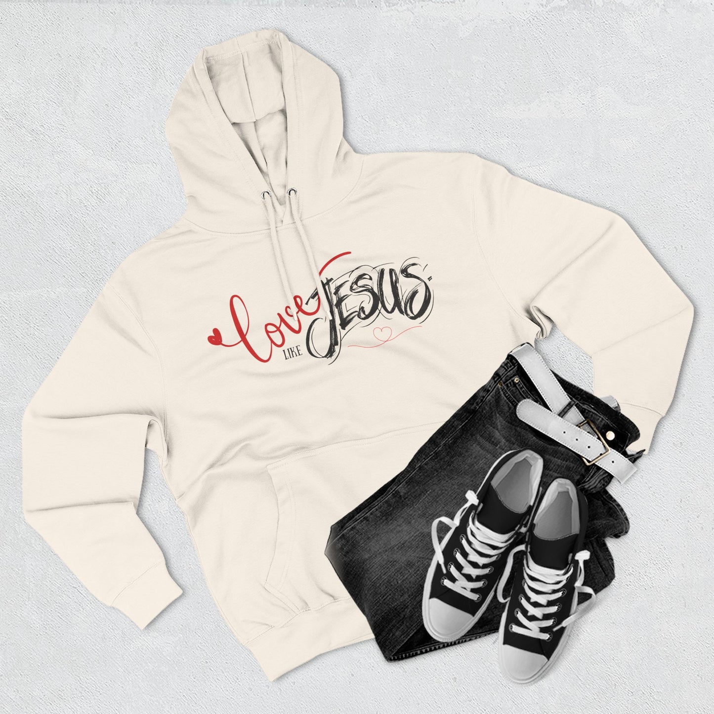 Beige hoodie with 'Love Jesus' text, black jeans, and black sneakers on a light gray background