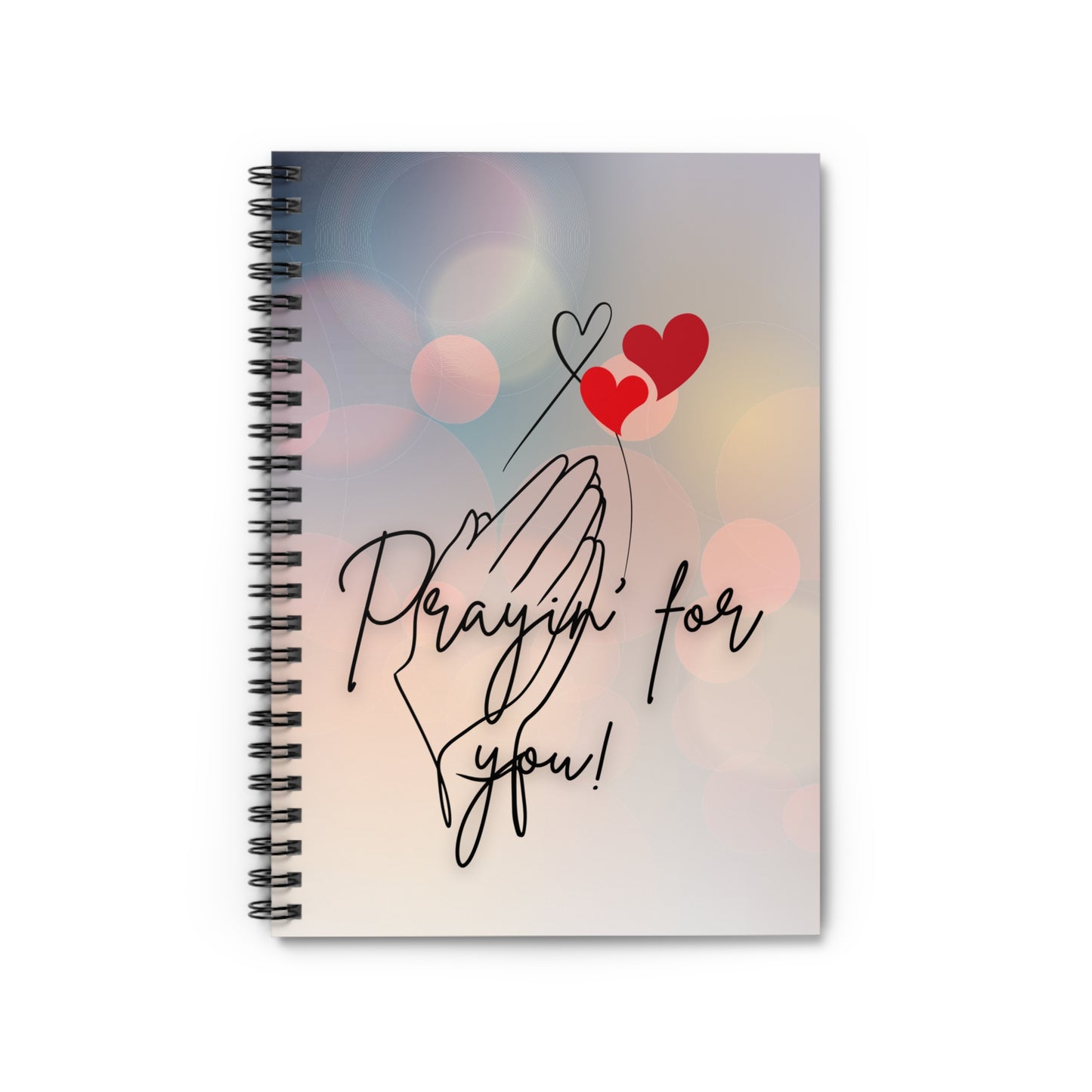 Notebook with 'Praying for you!' text and heart designs on a blurred background