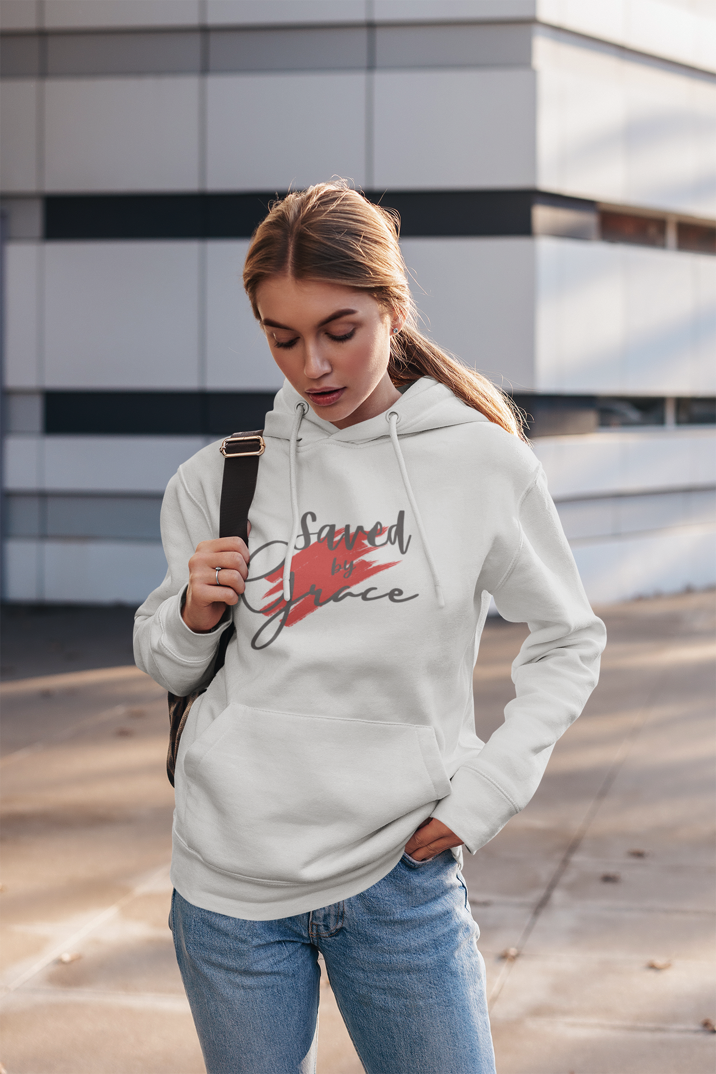 Woman wearing a white hoodie with a graphic design, standing outdoors.