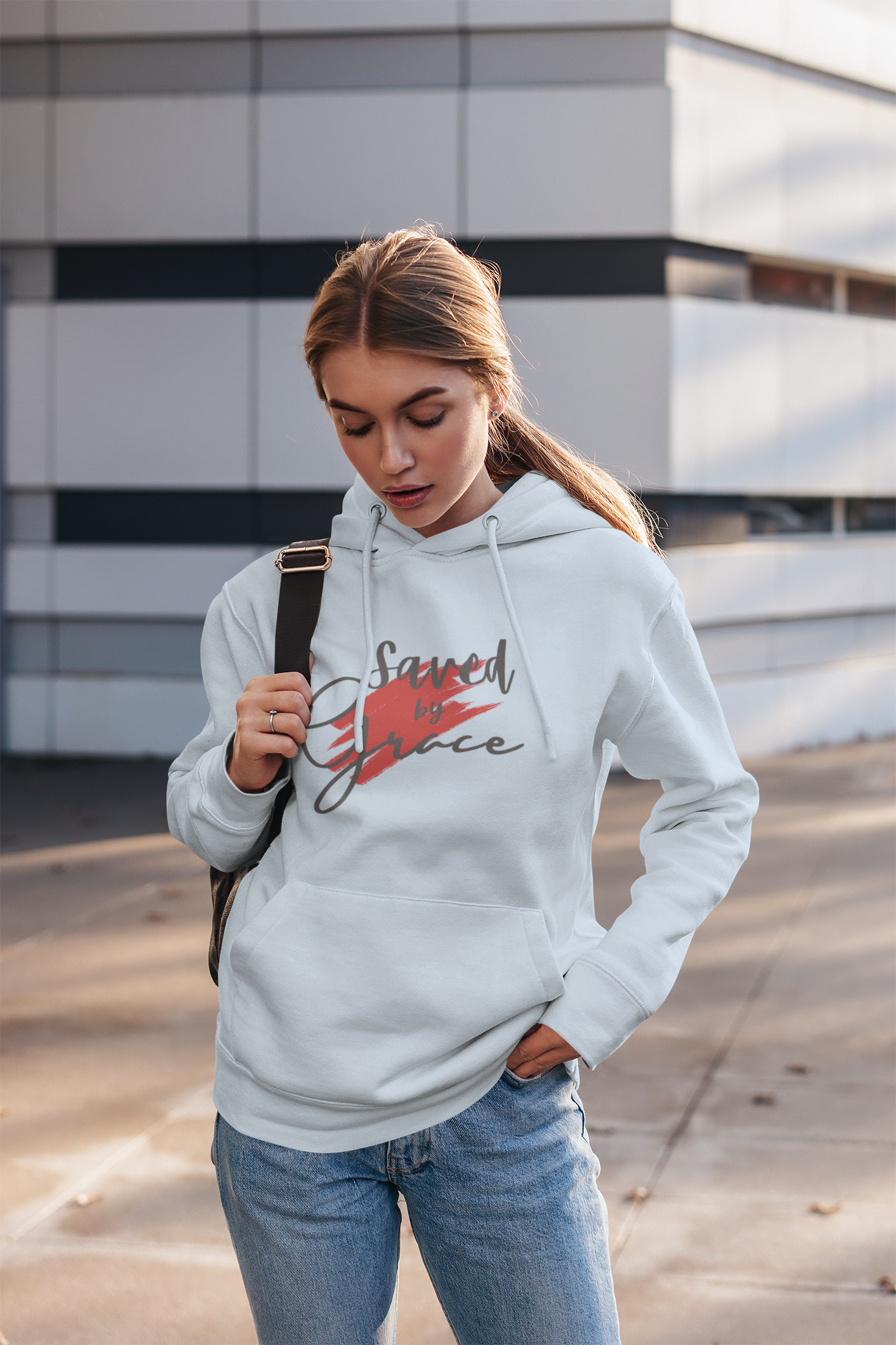 Woman wearing a white hoodie with text and design, standing outdoors.
