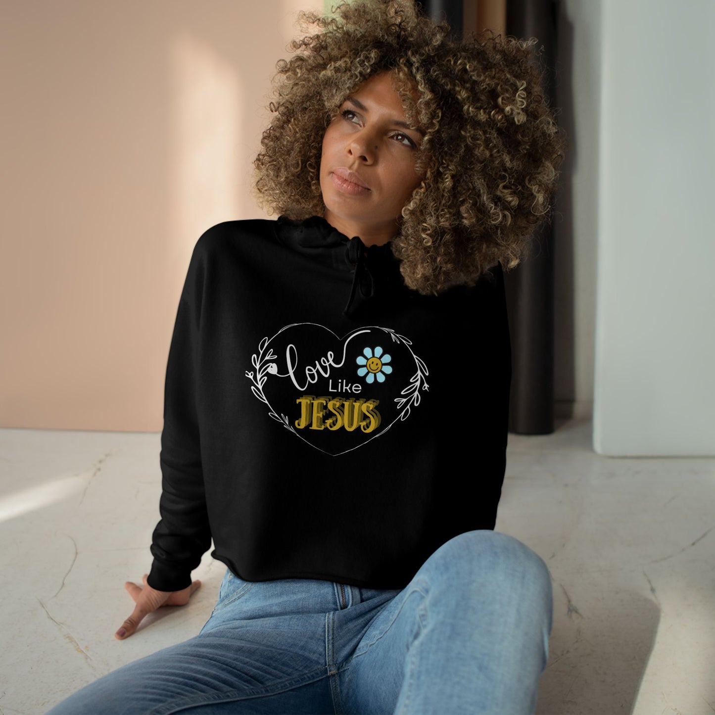 Woman wearing a black hoodie with 'Love Like Jesus' design, sitting on a light-colored floor.