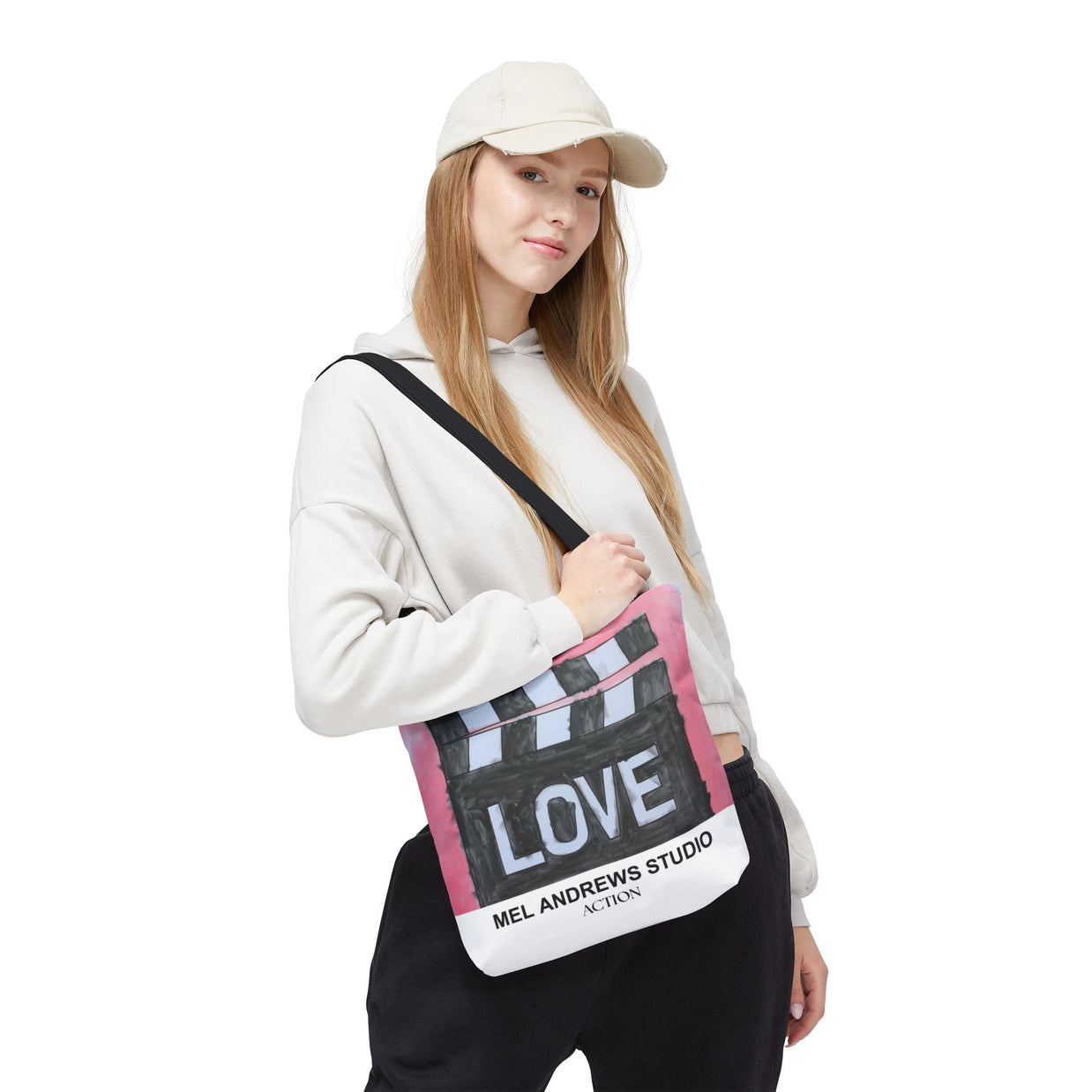 Person holding a tote bag with 'LOVE' and 'Mel Andrews Studio' text on a white background