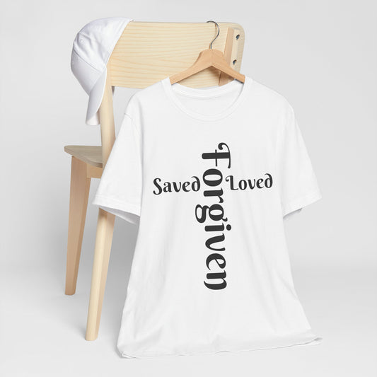 White t-shirt with 'Saved Loved Forgiven' text on a wooden chair against a white background
