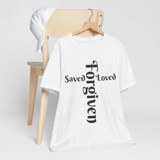 White t-shirt with 'Saved Loved Forgiven' text on a wooden chair against a white background