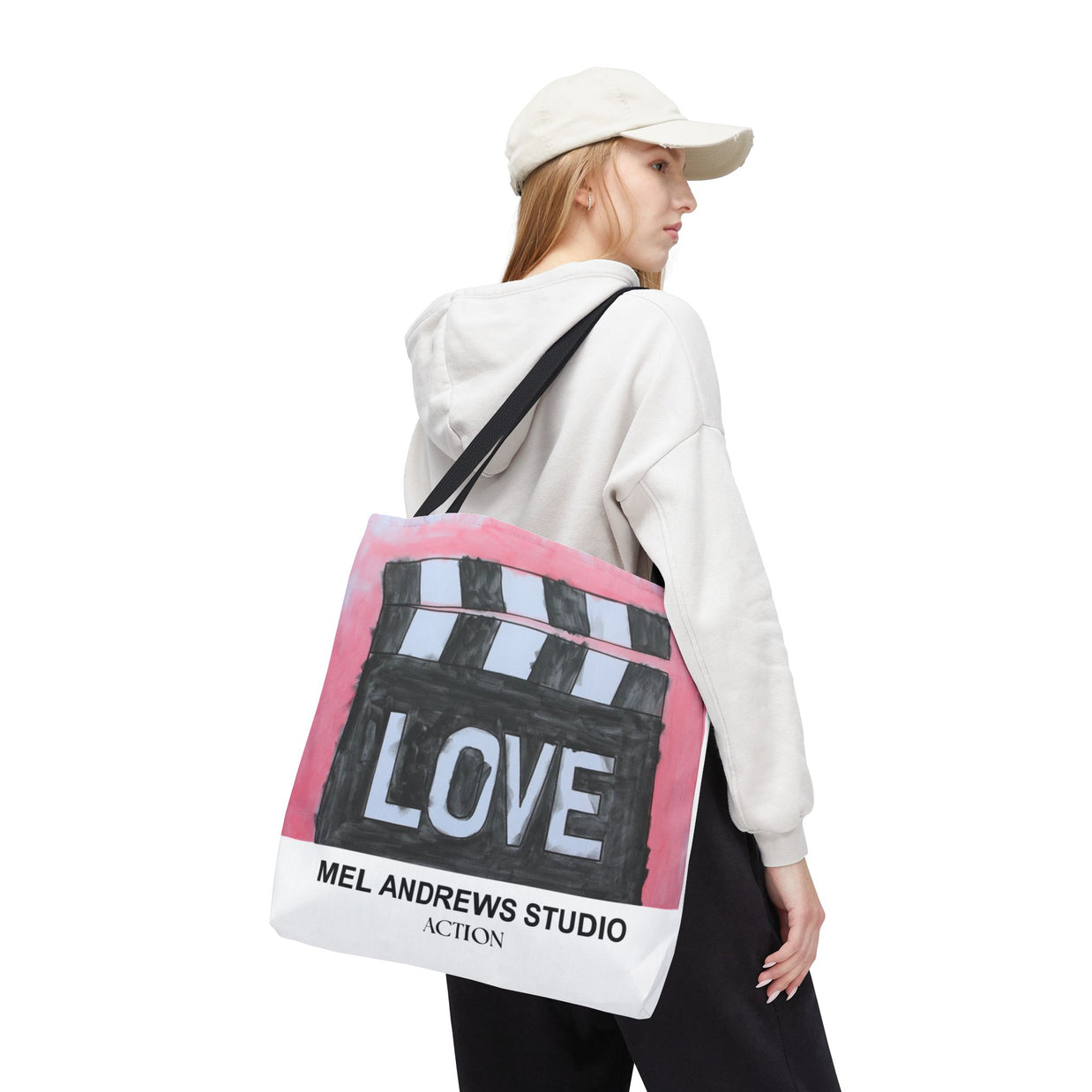 Person wearing a white hoodie and cap, carrying a tote bag with 'Mel Andrews Studio' branding.