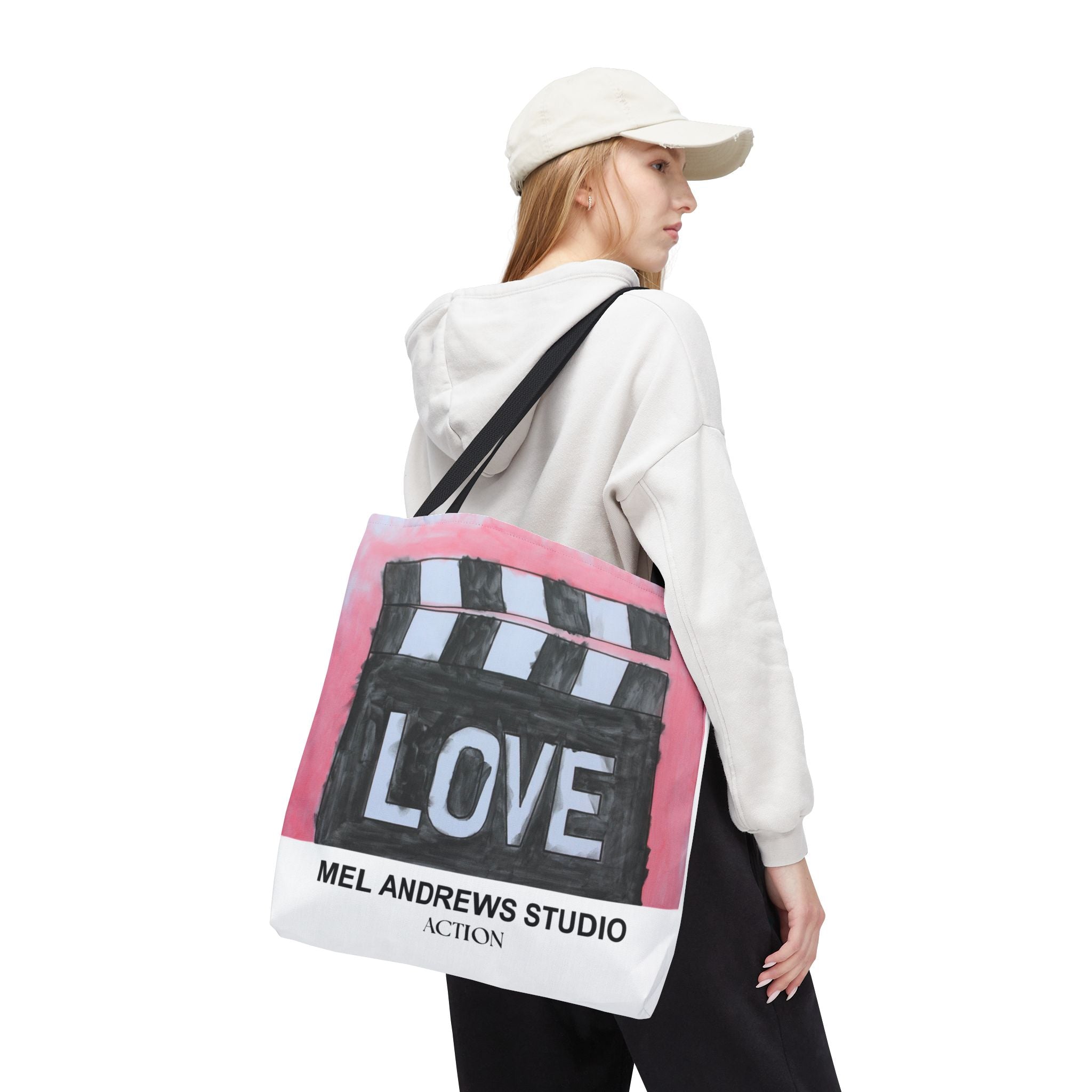 Person wearing a white hoodie and cap, carrying a tote bag with 'Mel Andrews Studio' branding.