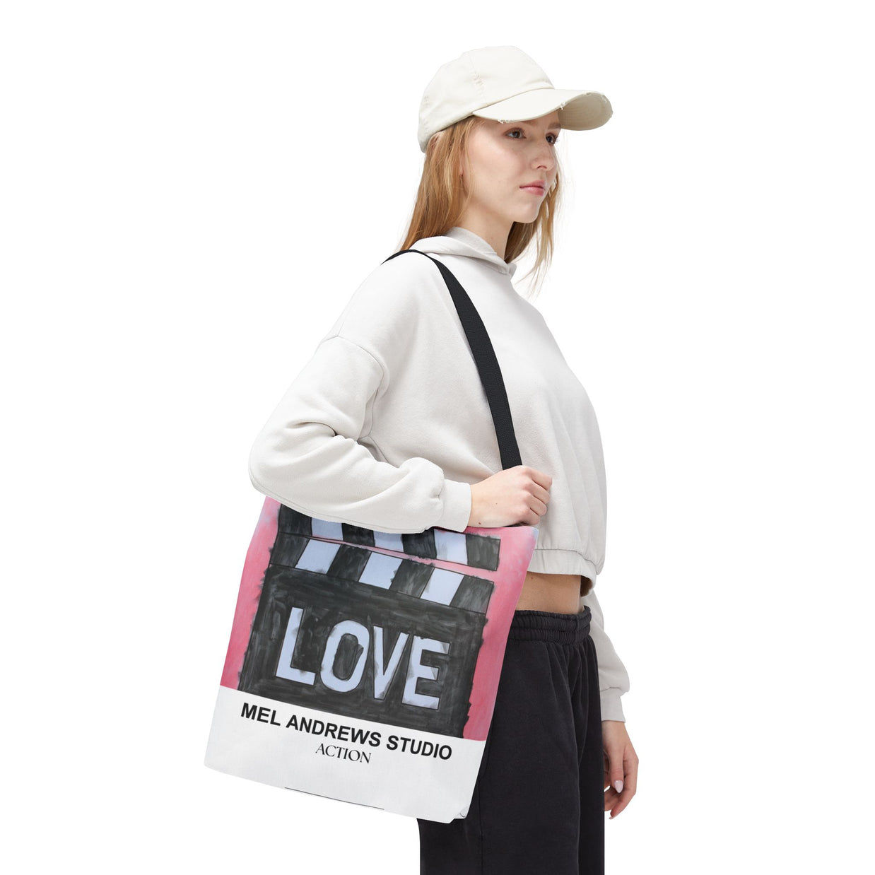 Person holding a tote bag with 'LOVE' and 'Mel Andrews Studio' text on a white background
