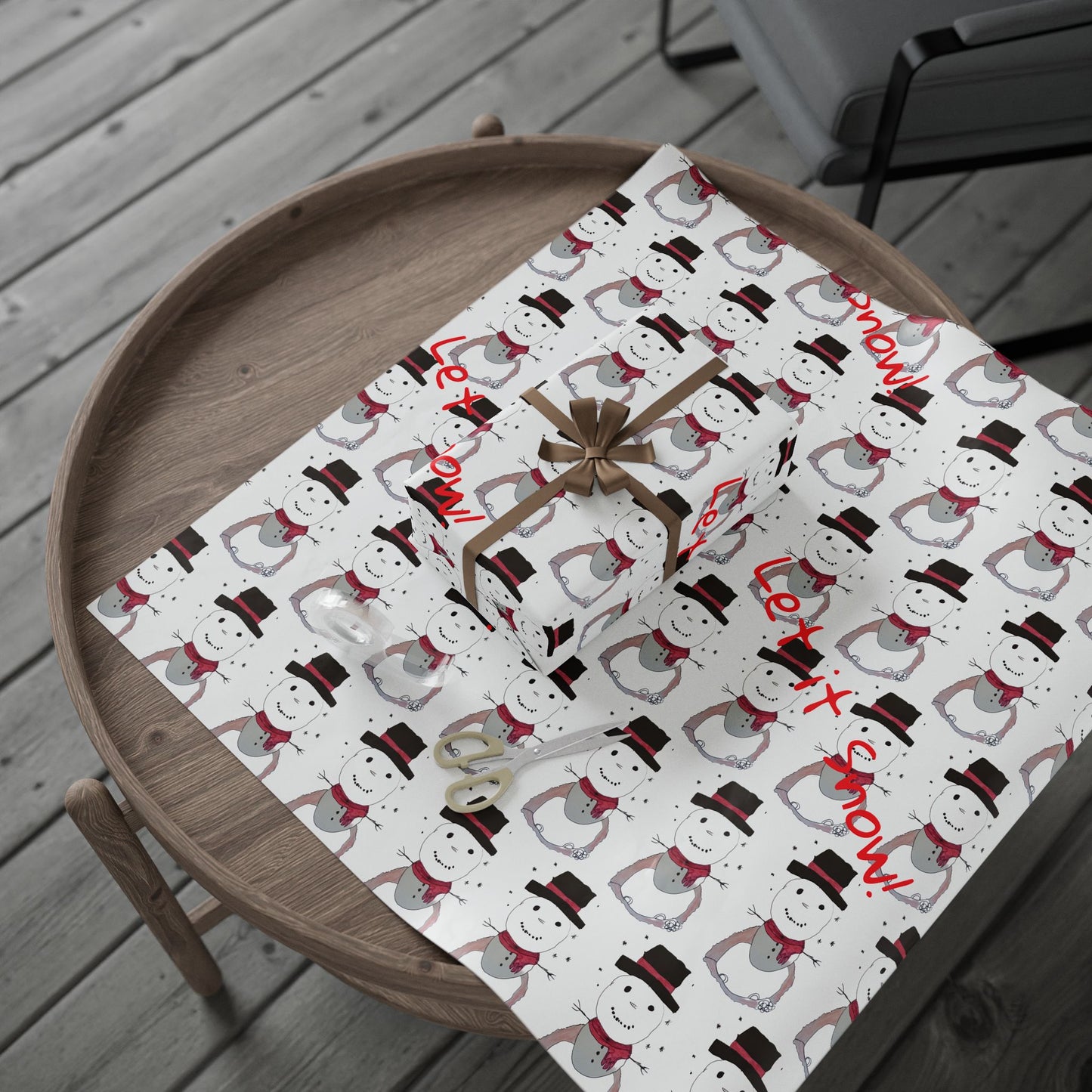 Christmas-themed gift wrap with snowmen and 'Let it snow!' text on a wooden surface.
