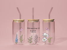 Three clear tumblers showing sides and front with floral designs and gold lids on a pink background