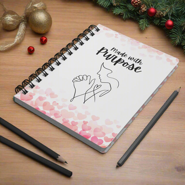 Notebook with 'Made with Purpose' text and heart design on a desk with pencils and a plant.