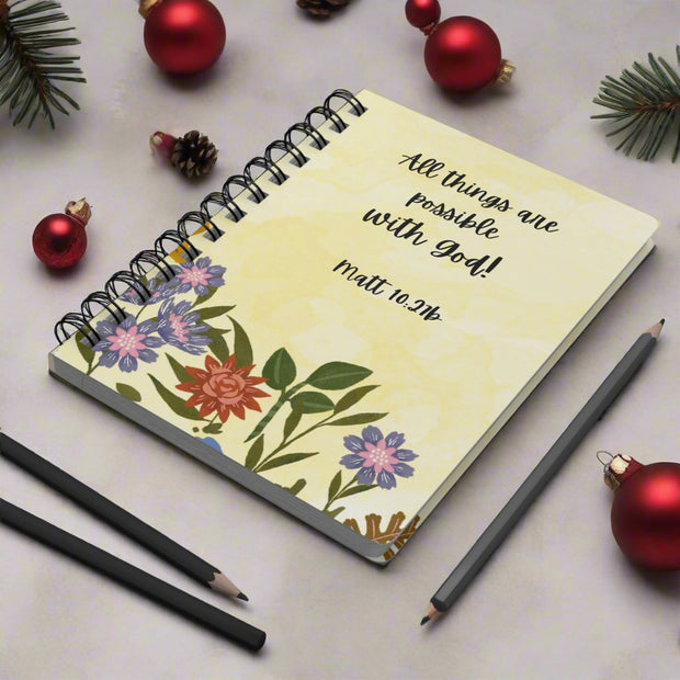 Notebook with floral design and a Bible verse on a desk with stationery items.