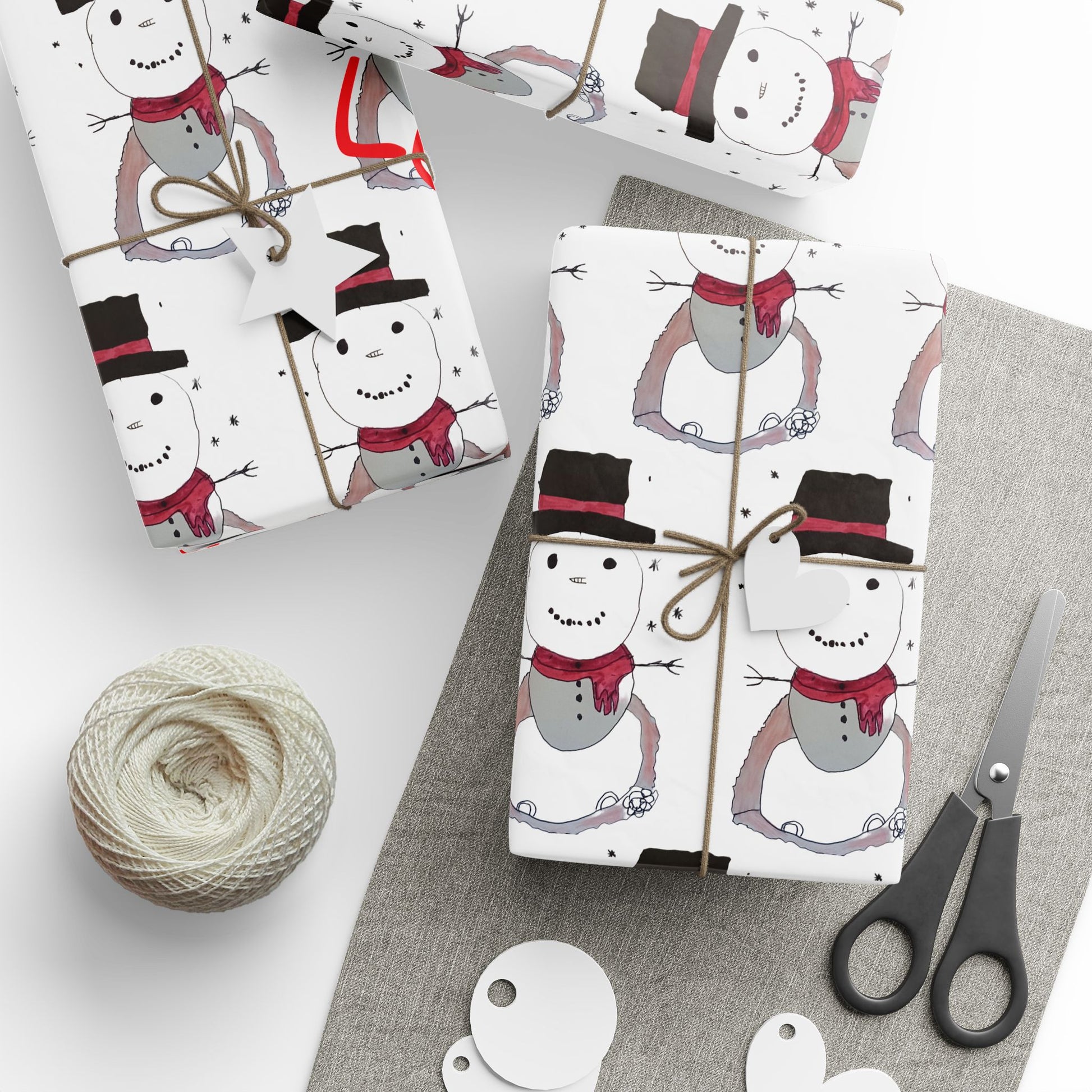 Gift wrap with snowman design, scissors, and string on a white surface