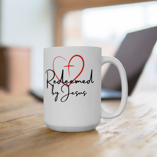 White mug with 'Redeemed by Jesus' text and red heart design on a wooden surface.